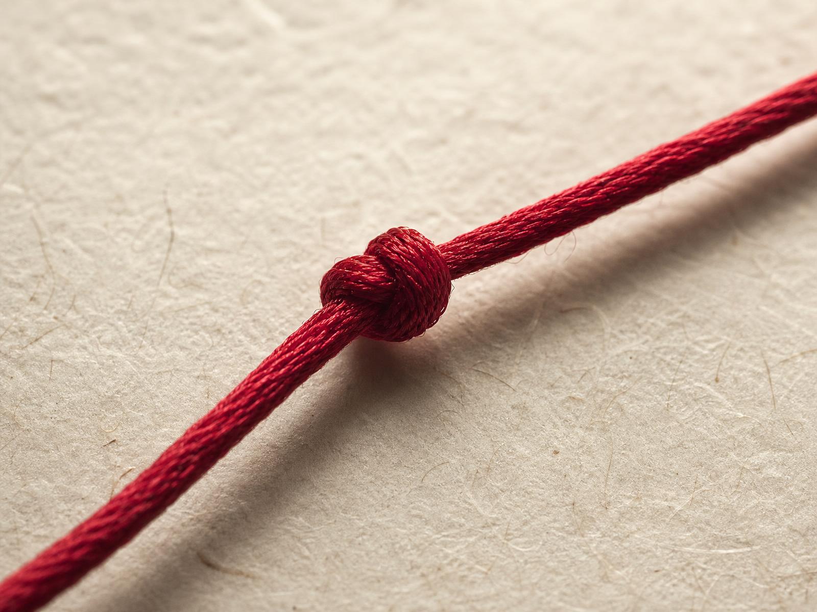 A crimson silk thread tied in a precise knot on handmade paper — a quiet symbol of connection between Europe and Greater China